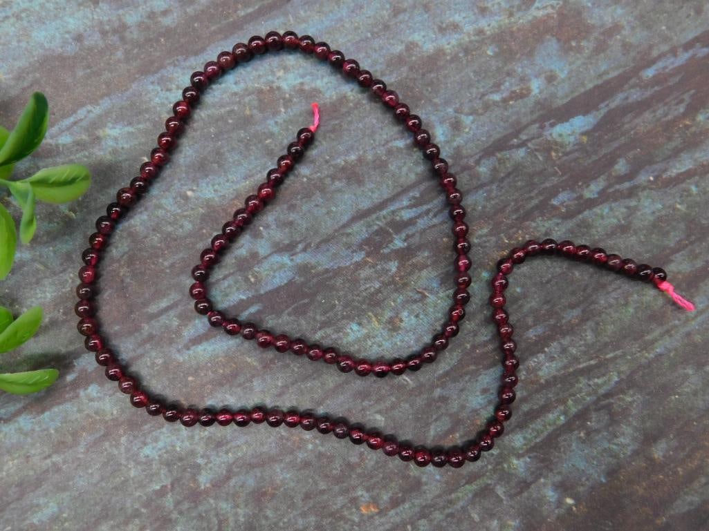 Strand of Garnet Beads: This lot features deep red round beads. Each bead appears uniformly shaped and polished, contributing to the smooth luster of the piece. The beads are strung tightly on a cord with visible knots and a