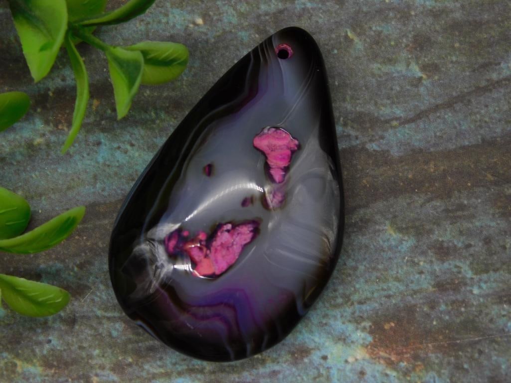 Polished Teardrop Black Agate Pendant with Pink Inclusions: Unique polished teardrop black agate pendant featuring vivid pink inclusions on the front. Smooth multi-tonal black and mauve surface with natural banding patterns on the back. Crafted with a drilled