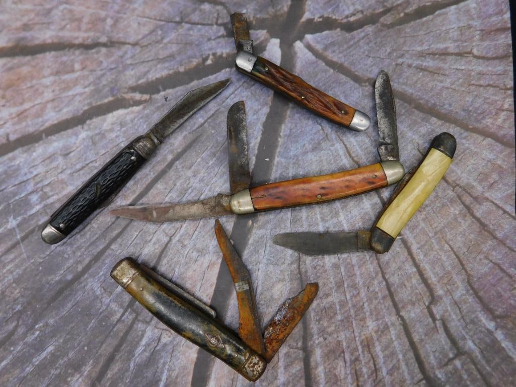 Lot of Five Folding Pocket Knives With Various Handles: Lot includes five folding pocket knives with diverse features. Handles include wood, bone, and metal. Some blades exhibit rust and wear, while other details like bolsters and rivets are visually intac