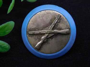Circular Military-Inspired Button Pin With Crossed Rifles Design