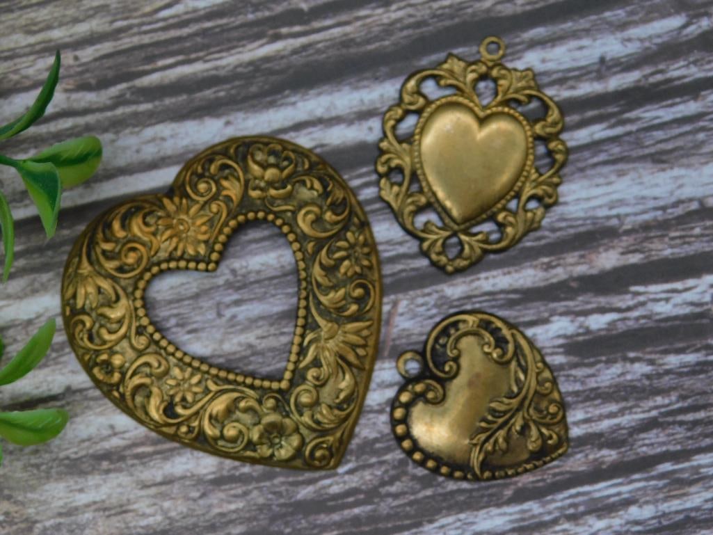 Set of Three Decorative Brass Heart Pendants: Set includes three heart-shaped brass pendants with detailed designs. Each pendant showcases intricate patterns, including floral and ornamental motifs. Two pendants are solid, and one features an ope