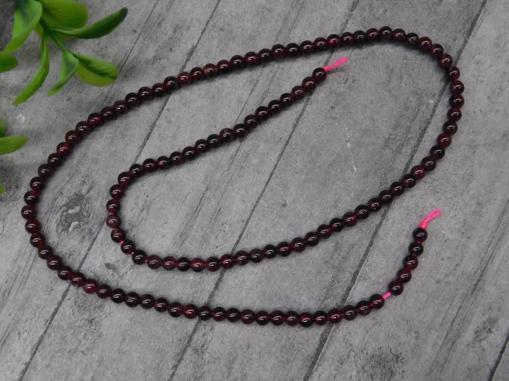 Strand of Polished Dark Garnet Beads for Jewelry Making: This strand consists of polished round beads in a rich dark red color. The beads are symmetrically strung on a pink cord, measuring approximately 18-19 inches in total length. Ideal for jewelry-making