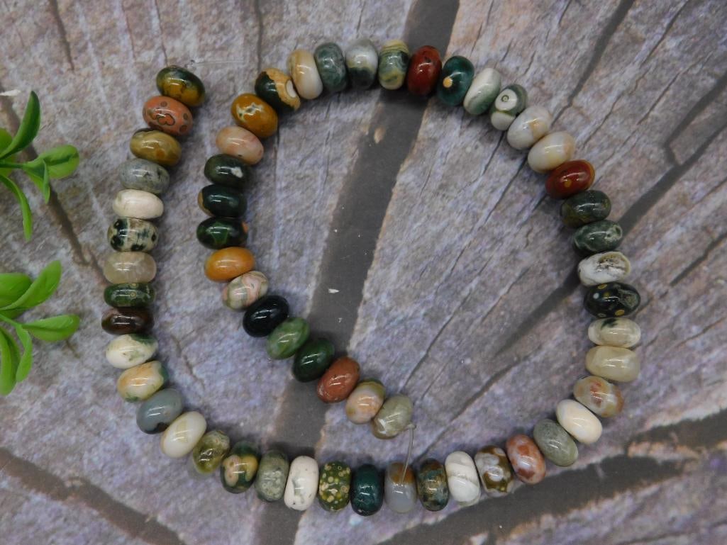 Multi-Colored Stone Beads: This lot includes a strand of multi-colored polished beads, possibly made of natural stone, such as jasper or agate. The beads are uniformly shaped and strung together. The item is displayed against a