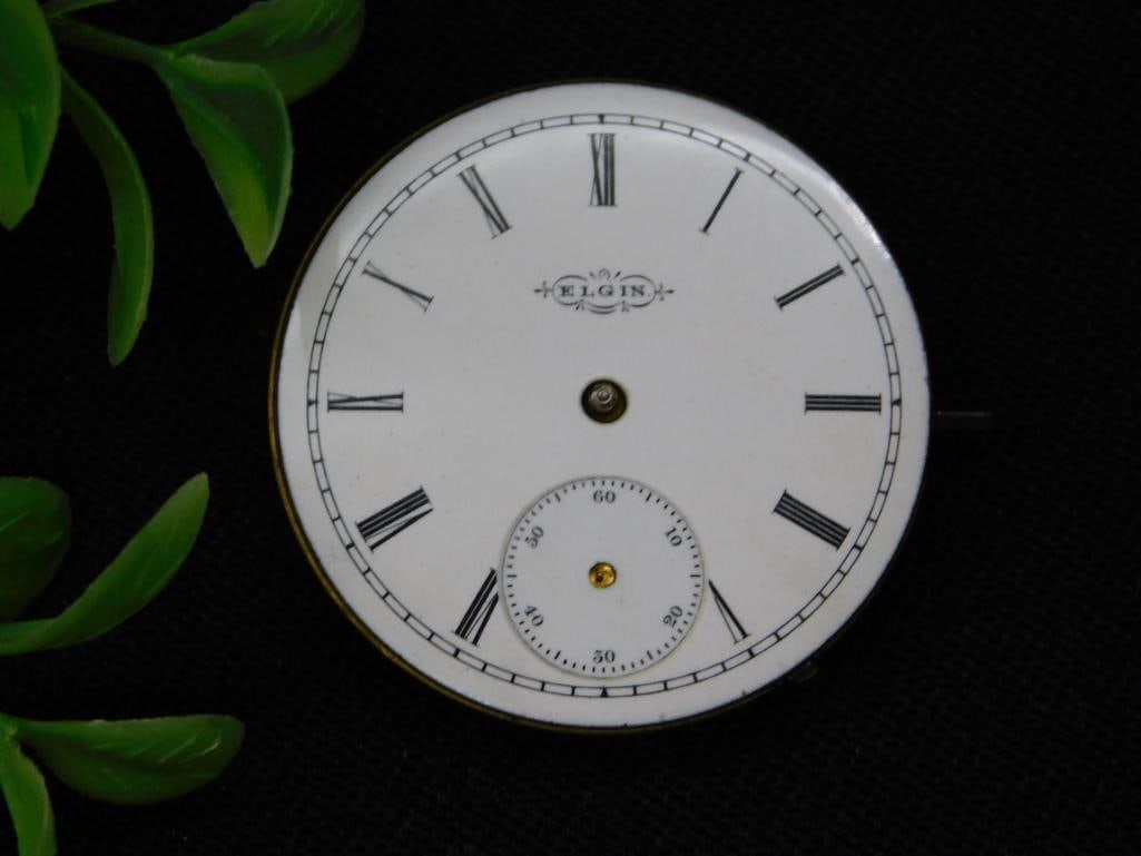 Elgin Pocket Watch Movement with Roman Numerals Dial WATCHMAKER WATCHMAKING TOOLS: - Circular Elgin pocket watch movement with a white enamel dial featuring Roman numerals and a sub-seconds dial. | - Movement marked with serial number '3888074' and intricate engravings. | - Includes
