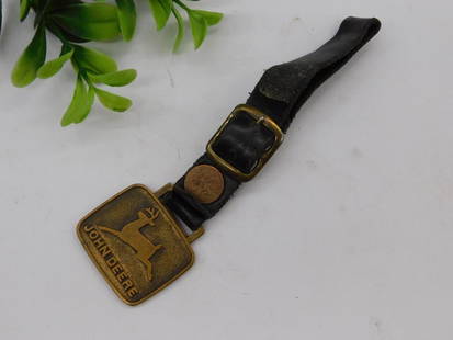 John Deere Watch Fob on Leather Strap WATCHMAKER WATCHMAKING TOOL: - Belt buckle featuring the John Deere logo with a leaping deer design and text "John Deere." | - Made with a metal buckle and attached to a leather strap. | - Adjustable strap with a metallic buckle