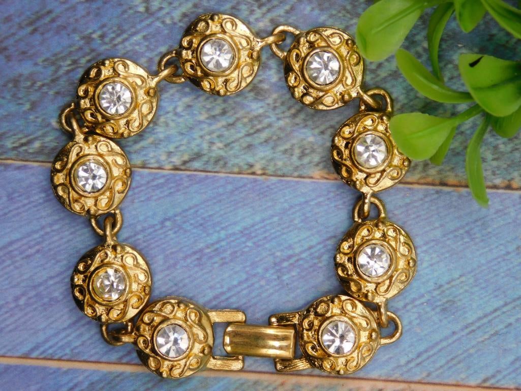 Gold-Tone Bracelet With Clear Stone Accents: - Gold-tone bracelet featuring circular links with raised dome designs. | - Each link is embellished with a large clear stone at the center. | - Secures with a fold-over clasp for easy wear. | - Appro