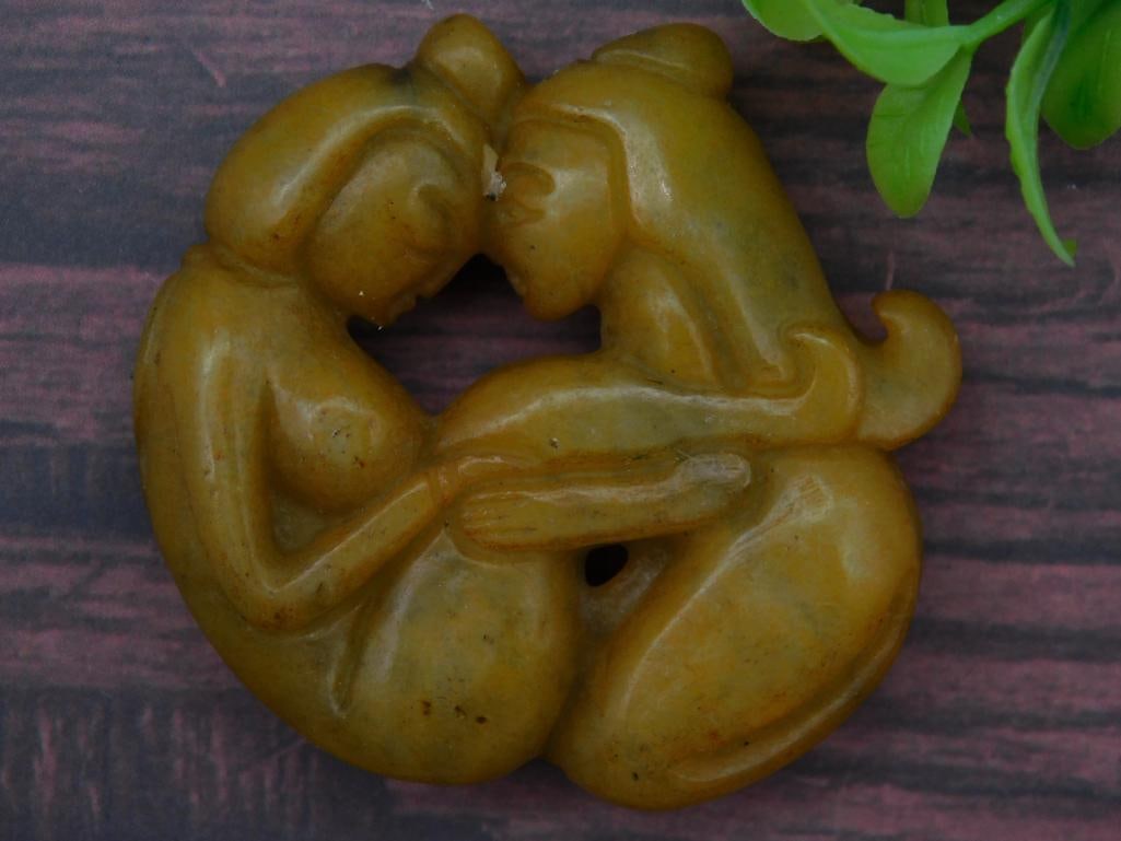 Carved Jade ROCK STONE LAPIDARY SPECIMEN: - Carved stone sculpture featuring two embracing human-like figures. | - Crafted from stone or similar material in a warm yellow-brown tone. | - Hole in the center, potentially for display or decorati
