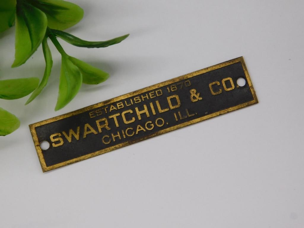 Swartchild & Co. Metal Plate Established 1870: Metal plate with text reading "Swartchild & Co., Established 1870, Chicago, Ill." | Two small holes on either end for mounting purposes | Rectangular shape with black background and gold lettering | D