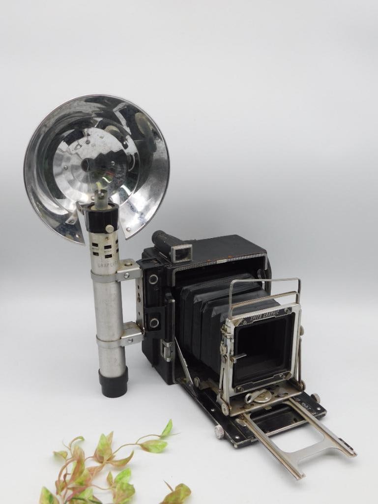 Graflex Speed Graphic Camera with Flash Attachment: This is a Graflex Speed Graphic large format 4x5 camera. The unit includes a flash attachment and features a bellows design for adjustable focal distance. The camera frame shows measurement markings f