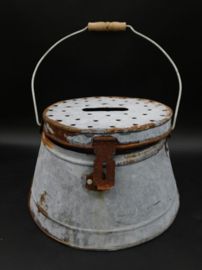 Metal Minnow Bucket with Perforated Lid and Handle: This item is a metal bucket featuring a perforated lid with a central opening and a latch closure. It includes a wire handle with a wooden grip for easier handling. The metal shows signs of rust and w