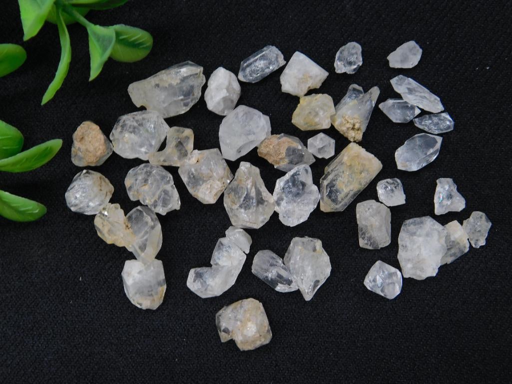 Herkimer Diamonds Rock Stone Lapidary Specimen: A collection of unpolished rough quartz specimens in varying shapes and sizes. Includes a total of 21 pieces. The pieces appear unrefined with natural inclusions and earth material. Ideal for collecto