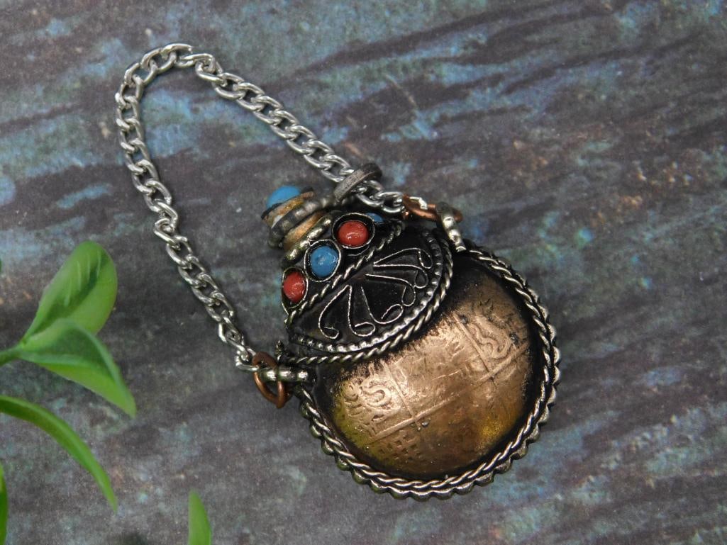 Small Ornamental Metal Snuff Bottle Pendant with Chain: This small ornamental flask pendant features a combination of metal and decorative details with inset red and blue stones. It includes a chain for hanging or wearing and a stopper attached by a cord.