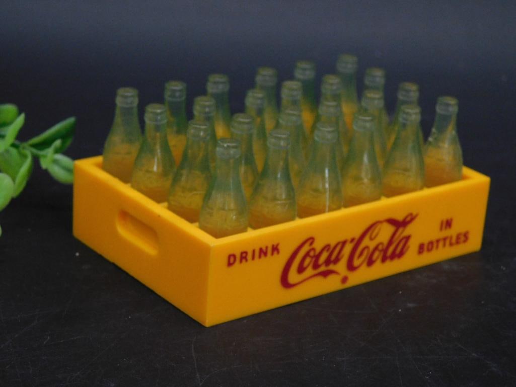 Vintage Coca-Cola Miniature Crate With Bottles: - Vintage Coca-Cola miniature crate set with small plastic bottles. | - Yellow plastic crate marked with Coca-Cola logo and 'Drink Coca-Cola in Bottles' text. | - Includes multiple translucent green b