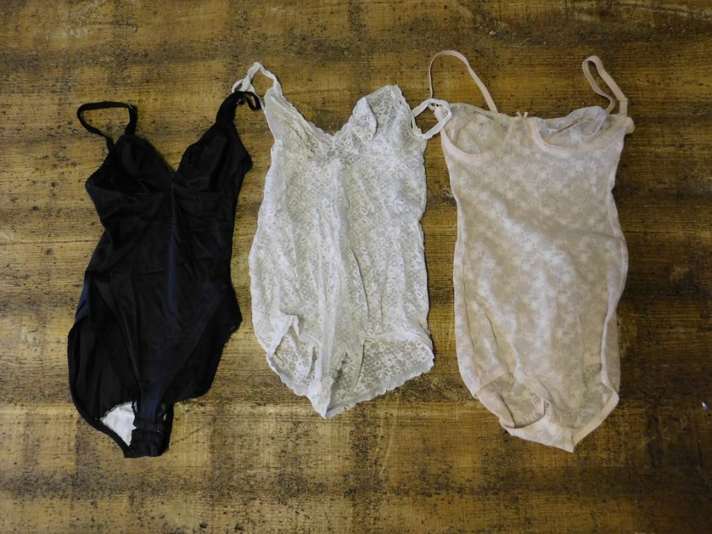 Lot of Three Women?s Lace Bodysuits in Various Colors: This lot includes three women's lace bodysuits in different colors: black, white, and beige. Each piece features adjustable straps and lace fabric construction. Sizing information visible on the w