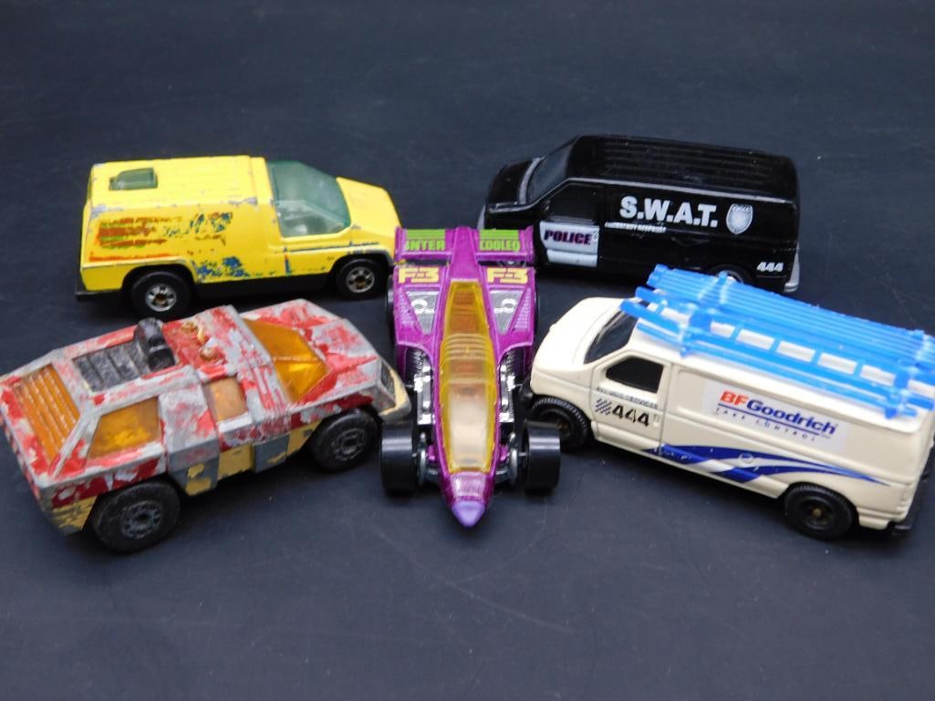Lot of 5 Die-Cast Toy Vehicles From Matchbox and Hot Wheels: This lot includes five die-cast toy vehicles featuring various designs. Items include: a Matchbox Ford Panel Van (1989), a Hot Wheels dragster (1977), a yellow van, a camouflage truck, and a SWAT van.
