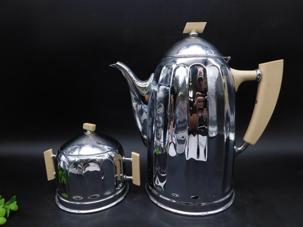 Vintage Belgian Chrome Teapot and Sugar Bowl Set: - Vintage chrome teapot and sugar bowl set. | - Crafted in Belgium with 'Belgium' and a maker's mark on the base. | - Features Bakelite handles and knobs in light cream color. | - Teapot includes a hi