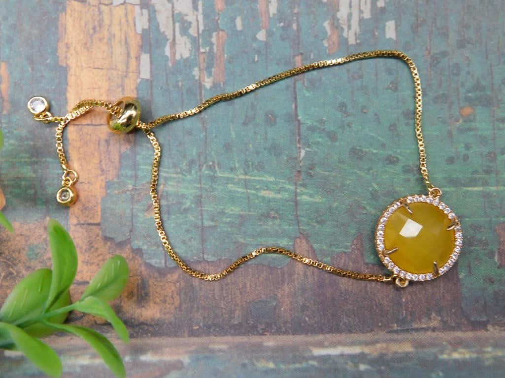 Adjustable Gold-Toned Bracelet With Yellow Gemstone: This adjustable gold-toned bracelet features a round yellow gemstone centerpiece surrounded by clear accent stones. The bracelet includes a sliding bead for custom fit adjustment. It has a simple chai