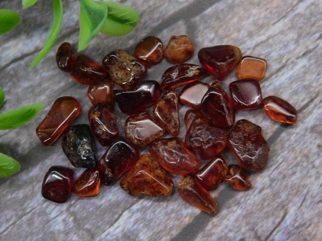 12 Grams of Orange Garnet Gemstones: A lot of 12 grams of orange garnet stones. These stones are tumbled and vary in shape and color intensity, displaying natural inclusions and polished surfaces. The size of the stones can be compared t