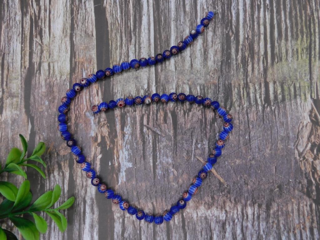 African Trade Beads Rock Stone Lapidary Specimen: This lot includes a single strand of blue and red millefiori glass beads. Each bead features intricate floral designs in vibrant colors set in a repeating pattern. The necklace measures approximately 
