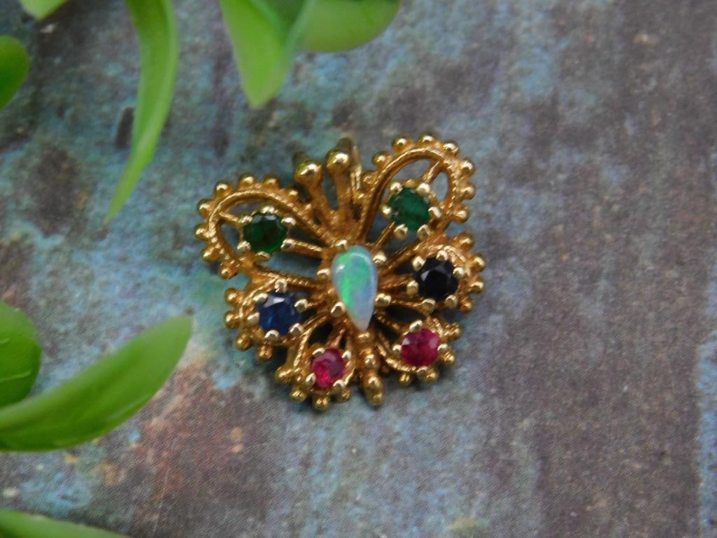 Gold-Tone Butterfly Brooch with Gemstone Accents: Gold-tone butterfly brooch featuring a central opal and accented with an array of colorful gemstone-like elements, including greens, blues, and reds. Unique open-framework design with scalloped edges.