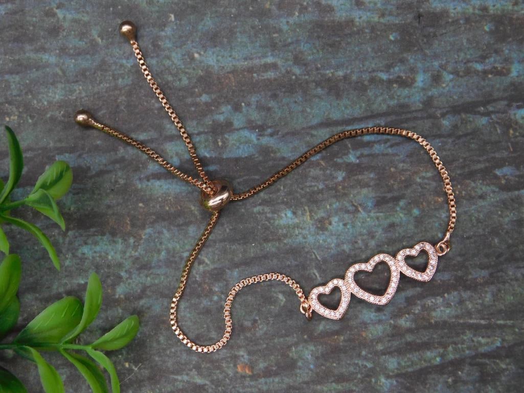 Rose Gold-Tone Bracelet With Triple Heart Motif: Delicate rose gold-tone bracelet featuring three heart-shaped elements adorned with clear, sparkling stones. Adjustable chain with sliding clasp ensures a customizable fit. Perfect as a statement piec
