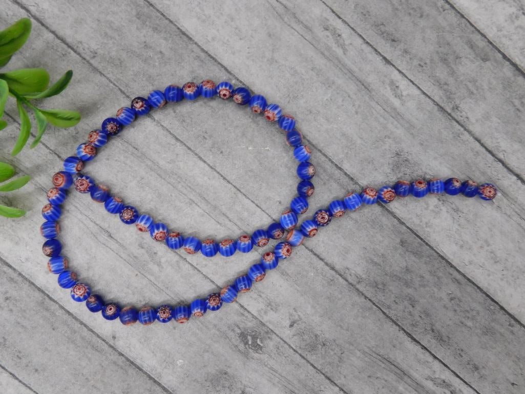 African Trade Beads Strand of Blue and Red Beads: This listing features a strand of vibrant blue and red millefiori glass beads. Each bead is detailed with floral patterns, showcasing intricate craftsmanship. The beads are uniformly strung and displa