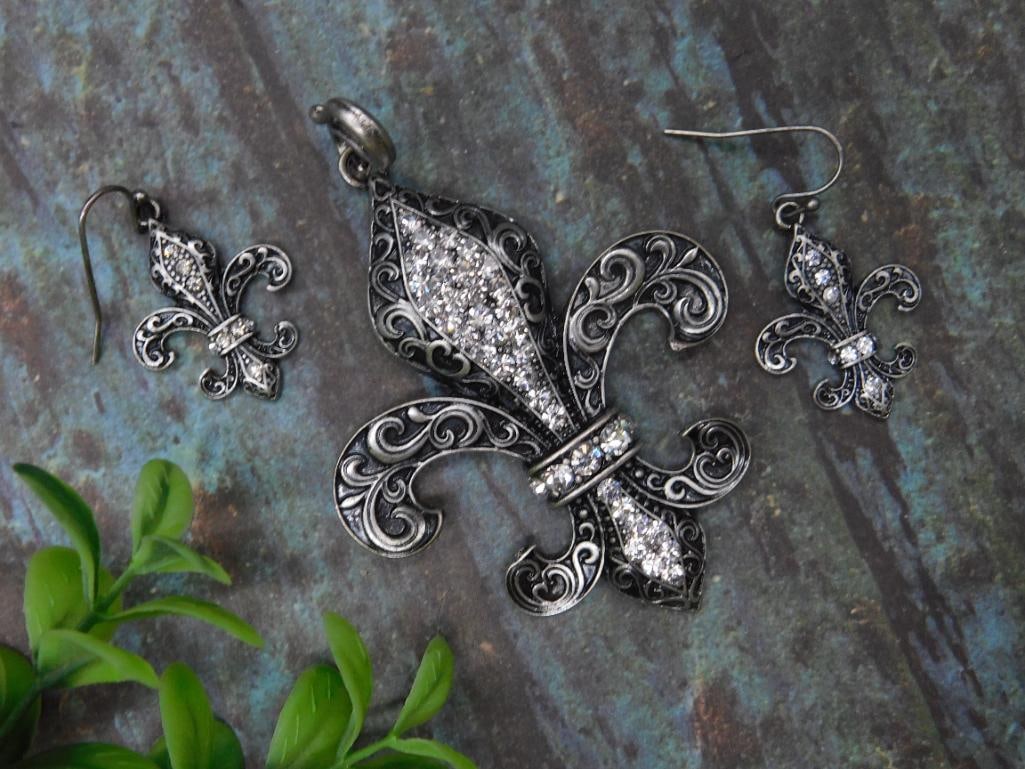 Fleur-de-Lis Jewelry Set with Pendant and Earrings: Elegant fleur-de-lis jewelry set, including one pendant and one pair of matching earrings. Each piece features an intricate filigree design and is adorned with sparkling clear stones. The set is craft