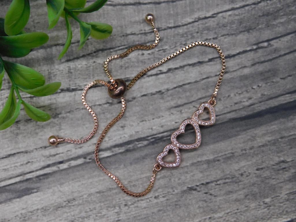 Rose Gold-Tone Bracelet With Heart Accents: Rose gold-tone bracelet featuring an adjustable chain with a sliding clasp for a custom fit. Accented with three open heart-shaped designs encrusted with round clear stones for added sparkle. A stylis