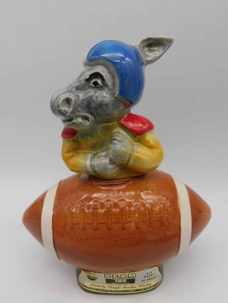 Jim Beam Kentucky Bourbon Donkey Football Decanter: - Vintage Jim Beam decanter crafted from genuine Regal China. | - Features a donkey wearing a blue helmet and yellow jersey, positioned atop a football. | - Includes original label indicating contents