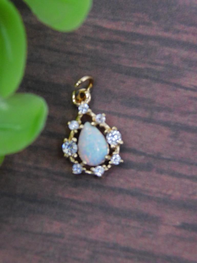 Gold-Tone Pendant With Opal and Clear Stones: Gold-tone pendant with a tear-drop shaped opal centerpiece. | Surrounded by a decorative arrangement of clear, round-cut stones. | Features a loop for easy attachment to a chain or jewelry piece. | Co