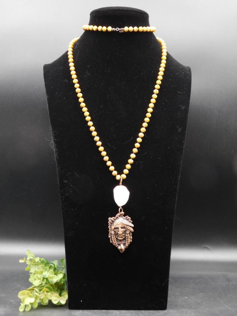 Beaded Necklace With Native American-Inspired Pendant: Handcrafted necklace featuring yellow beads throughout the chain | Central pendant with a Native American-inspired design in bronze-tone metal | White stone-like element above the pendant, adding cont