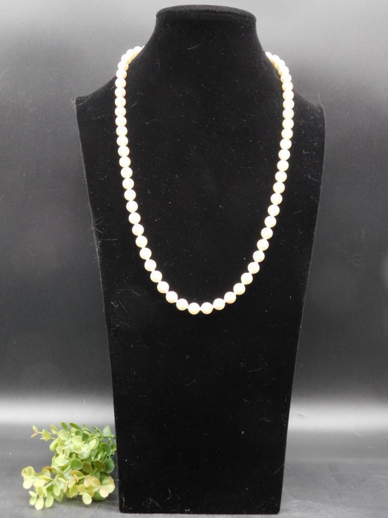 Classic Strand of White Pearl Beads Necklace: Elegant strand of white pearl-style beads. | Appears uniform in bead size and shape, with a smooth finish. | Versatile length offering potential for layering or standalone wearing. | Displayed on a bl