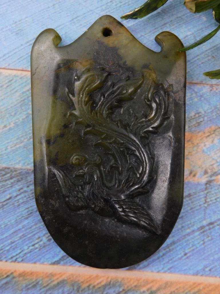 Antique Carved Jade Pendant with Floral Design Rock Stone Lapidary Specimen: Carved jade pendant featuring a floral design motif. | Material: Appears to be green-colored jade. | Approximate size shown next to a ruler for scale. | Features a hole at the top for use as a pendant