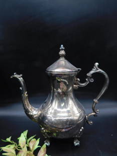 Silver-Plated Teapot With Hinged Lid: Silver-plated teapot featuring ornate handles, a hinged lid, and decorative feet. Moderate tarnishing visible, suitable for restoration or cleaning.