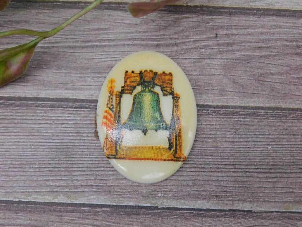 Oval Liberty Bell Decorative Cabochon with Patriotic Theme: Oval-shaped decorative cabochon featuring an illustration of the Liberty Bell framed with an American flag motif. Measures approximately 2 inches in height, as shown next to a ruler. Suitable for craf