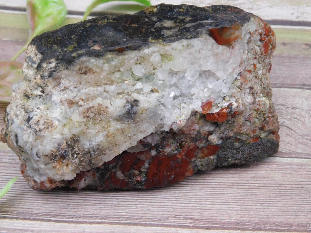 Quartz and Red Mineral Specimen with Rough Exterior: This specimen consists of a quartz-infilled geode-like formation with dark exterior and red mineral inclusions visible within the matrix. The rough-cut mineral piece weighs approximately 269 grams, as