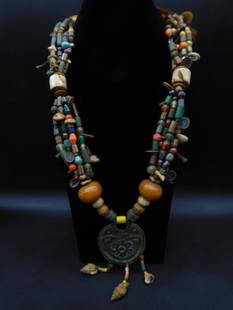 AFRICAN TRADE BEAD Necklace With Pendant and Shell Dangles: This multi-strand necklace features an array of colorful, variously shaped beads, including stone and glass. The necklace showcases a central large circular pendant with intricate floral detailing and