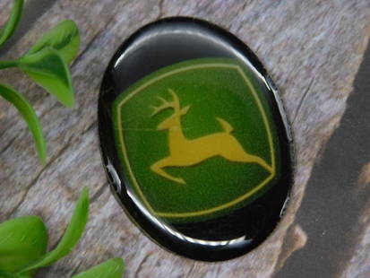 John Deere Emblem Cabochon: Round glass cabochon featuring a John Deere emblem. Design includes the iconic deer logo in green and yellow. Approximate size shown next to a U.S. quarter for scale. Perfect for craft, jewelry, or co