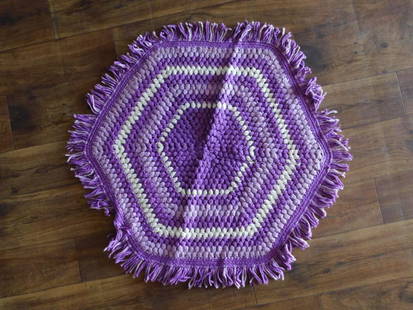 Handmade Purple and White Hexagonal Crochet Rug: This handmade hexagonal crochet rug features a purple and white design with a fringe border. The rug is crafted using a crochet technique, showcasing alternating light and dark purple hues with white