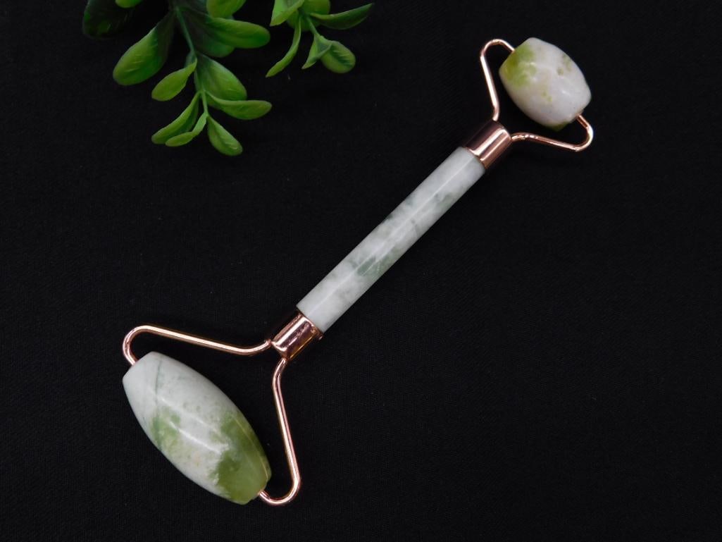 Dual-Ended Jade Facial Roller with Gold-Tone Frame: Dual-ended jade facial roller featuring two polished, naturally green and white stones for facial massage. The roller is set in a gold-tone frame with a smooth cylindrical grip and designed for skinca