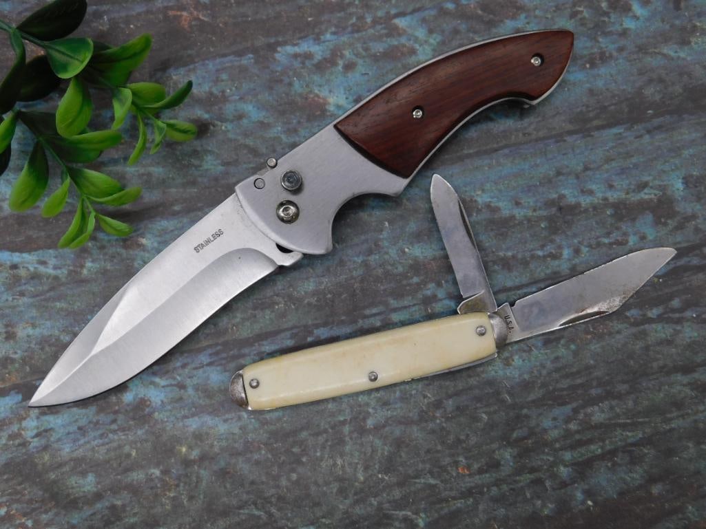 Set of Two Folding Knives with Wood and Synthetic Handles: This lot includes two folding knives. The first knife features a stainless steel blade with a wooden handle, while the second knife is a smaller folding pocket knife with a cream-colored synthetic han