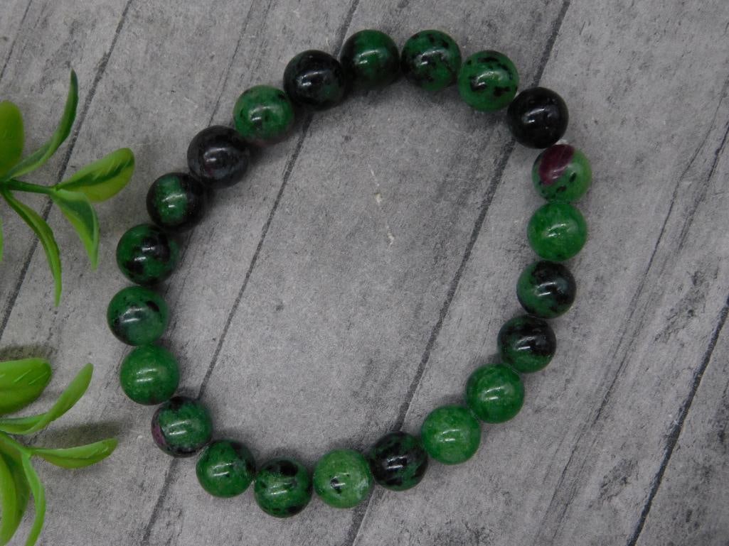 Elastic Bracelet With Green And Black Beads: Elastic bracelet featuring green and black round beads. Beads are uniform in size with a polished finish. Suitable for a range of wrist sizes due to its elastic design. Includes a coin in the image fo