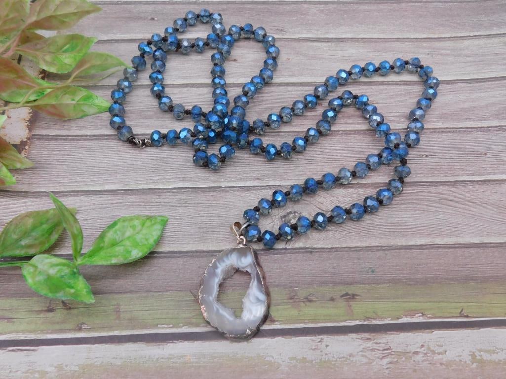 Faceted Blue Beaded Necklace With Agate Pendant: A faceted blue beaded necklace featuring a natural agate pendant. The necklace is strung with consistently shaped blue beads finished with a gold-tone detail around the pendant. Includes a measurement