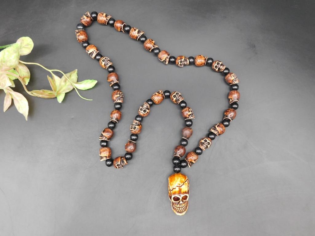 Hand-Carved Skull Pendant Necklace With Beaded Chain: This striking necklace features a hand-carved skull pendant paired with a bead chain made of wood and black beads. Skulls are intricately carved on the wooden beads. The necklace is noticeably detaile