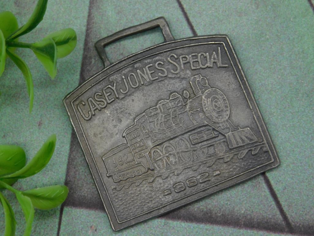 Casey Jones Special 1982 Watch Fob: Metal belt buckle featuring a depiction of a train with text reading ?Casey Jones Special? and ?1982.? The buckle exhibits a square-shaped top with an embossed design, suitable for attachment to a bel