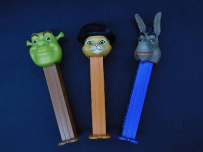 Set of Three Shrek-Themed PEZ Dispensers: This lot includes a set of three PEZ dispensers featuring characters from Shrek: Shrek, Puss in Boots, and Donkey. Each dispenser showcases a character's head and is marked "Made in China" with U.S. P