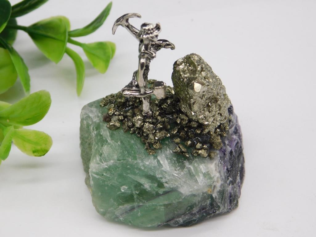 Pyrite Miner Figurine on Fluorite Rock Stone Lapidary Specimen: - Decorative piece featuring a miner figurine mounted on a mix of green fluorite and pyrite. | - Includes detailed pyrite formations and a realistic miniature mining pick. | - Green fluorite forms the