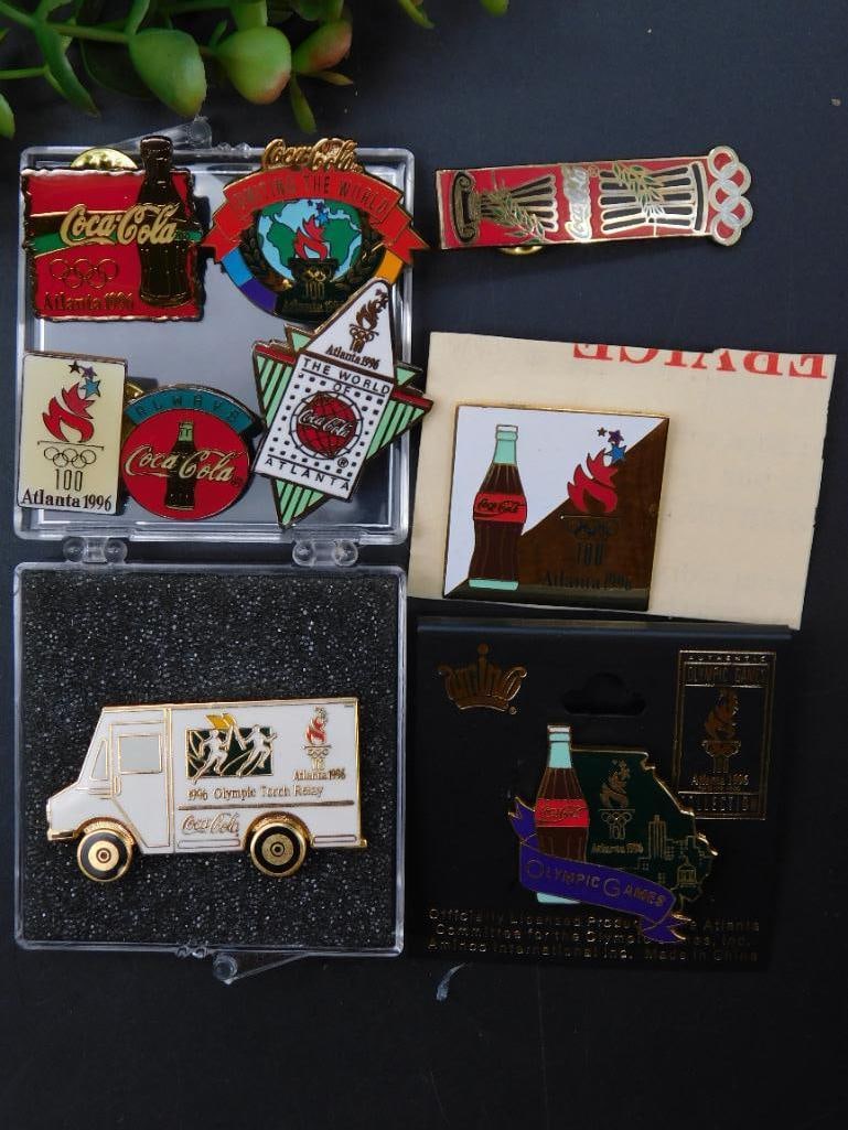Atlanta 1996 Olympic Games Coca-Cola Pin Collection: Collection of Atlanta 1996 Olympic Games Coca-Cola-themed pins. | Includes various designs featuring Coca-Cola branding, Olympic torch logo, and Olympic-themed graphics. | One pin shaped like a delive
