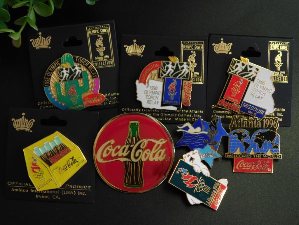 1996 Atlanta Olympics Coca-Cola Pin Collection: Collection of official Coca-Cola pins from the 1996 Atlanta Olympics. | Includes various designs, featuring the Olympic Torch Relay and Coca-Cola branding. | Pins represent locations such as Washingto