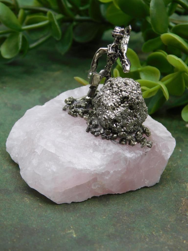 Miner Figurine on Rose Quartz with Pyrite Cluster Rock Stone Lapidary Specimen: Decorative figurine featuring a miner crafted from metal. | Positioned on a rose quartz base with an attached pyrite cluster. | Dimensions not specified; coin shown for size reference. | Unique combin